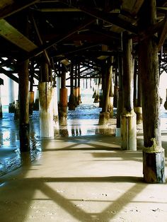 the underside of a pier with water under it and lots of wooden poles on either side