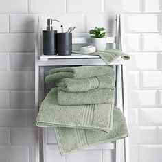 towels are stacked on a towel rack in the bathroom, with a plant and soap dispenser nearby