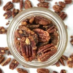 a glass jar filled with pecans on top of a white tablecloth covered in nuts