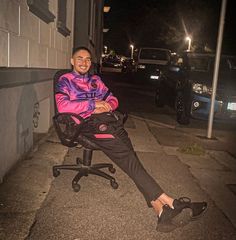 a woman sitting in an office chair on the sidewalk at night with her feet up