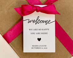 there is a gift wrapped in brown paper with a pink ribbon on it that says, welcome we are so happy you are here