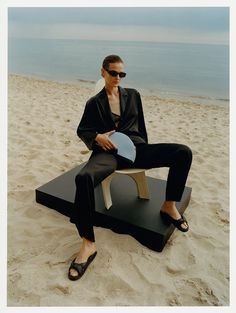 a woman sitting on top of a wooden table next to the ocean holding a paddle