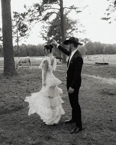 a man and woman dressed up in formal wear walking through a field with horses behind them