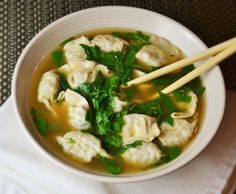 a white bowl filled with dumplings and green vegetables next to two chopsticks