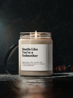 a candle sitting on top of a wooden table next to a black mug with the words smile like you're a godmother