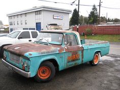 an old rusted pickup truck parked in front of a building with two other trucks behind it