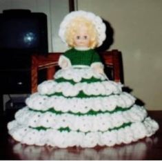 a doll sitting in a dress made out of crocheted yarn on top of a table