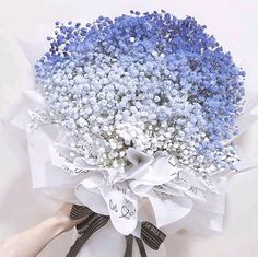 a bouquet of blue and white flowers is being held by someone's hand,