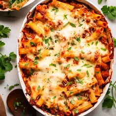 two bowls filled with pasta and sauce on top of a white table next to parsley