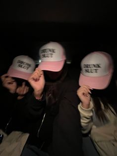 three people with hats covering their faces in the dark, one wearing a pink hat