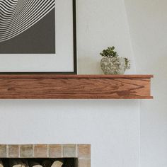 a white fireplace with wood mantle and framed art