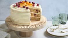 there is a cake with white frosting and fruit on top, next to two glasses