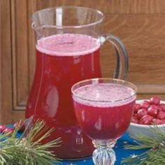 a pitcher of liquid next to a bowl of berries and pine cones on a table