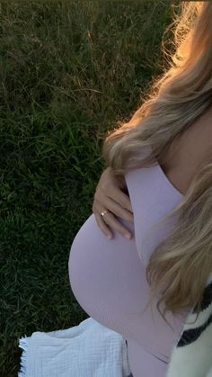 a pregnant woman sitting in the grass with her hand on her belly