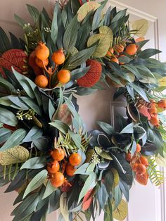 a wreath with oranges and leaves hanging on a door