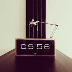 an alarm clock sitting on top of a wooden table next to a wall mounted lamp