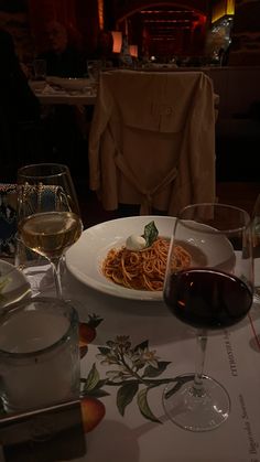 a plate of spaghetti and two glasses of wine on a table in a dimly lit room