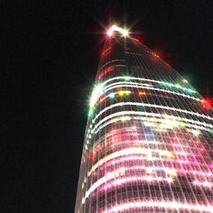 a very tall building with lights on it's side and the sky in the background