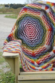 a multicolored crocheted blanket sitting on top of a wooden chair in the grass