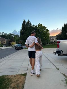 a man and woman walking down the sidewalk with their back to each other, hugging