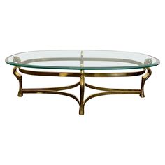 a glass and brass coffee table with an oval glass shelf on one end, and a metal frame around the top