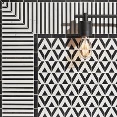 a black and white tiled wall with a light bulb on it's side in the middle