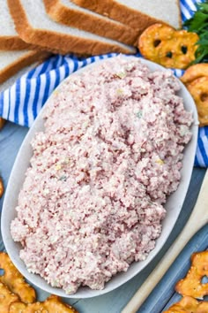 a white bowl filled with tuna salad next to crackers and pretzels on a table