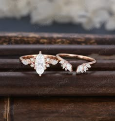 two gold rings with diamonds on them sitting on top of a wooden table next to flowers