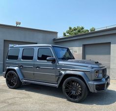 a silver mercedes g - class parked in front of a garage