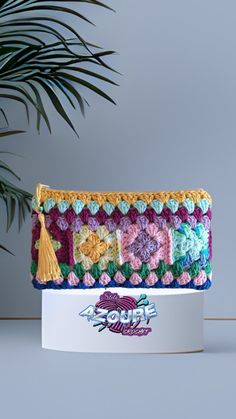 a colorful crocheted purse sitting on top of a white box next to a plant