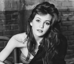 a black and white photo of a woman with long hair sitting on a chair in front of a brick wall