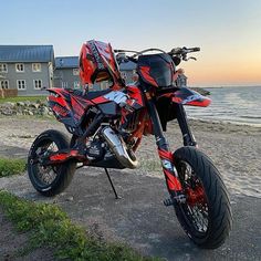 a red and black motorcycle parked on top of a dirt road next to the ocean