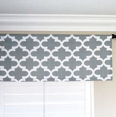 a gray and white window valance hanging on the side of a door with shutters