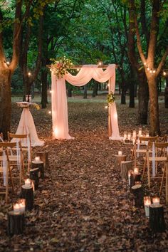 an outdoor wedding set up in the woods with candles and drapes on the ground