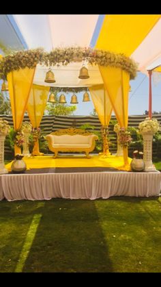 an outdoor wedding setup with yellow draping and flowers on the ground, surrounded by grass