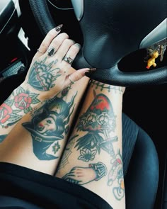 a woman with tattoos on her legs is sitting in a car and holding the steering wheel