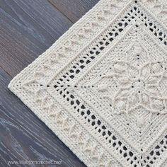 a white crocheted square on top of a wooden floor next to a black and white rug