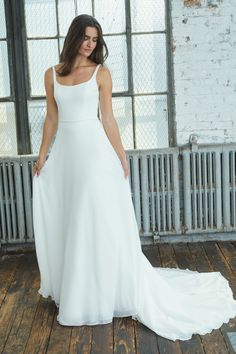 a woman in a white wedding dress standing on a wooden floor next to a window