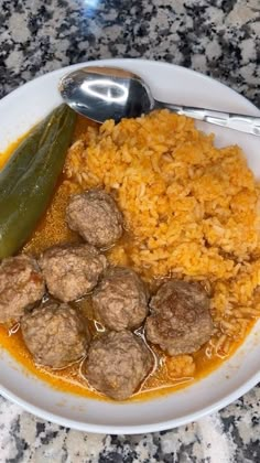 a white plate topped with meatballs and rice next to a pickle on top of a table