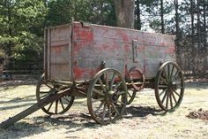 an old wooden wagon sitting on top of a grass covered field next to a forest