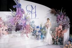 a woman in a white dress standing next to flowers on a stage at a fashion show