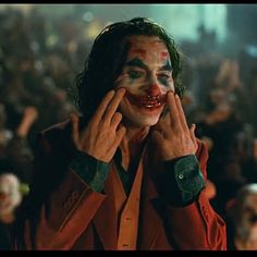 the joker is holding his hands to his face as he stands in front of an audience