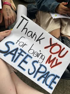 a person sitting on the ground holding a sign that says thank you for being my safe space