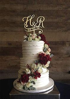 a white wedding cake with red and white flowers on the top tier is displayed against a wooden wall