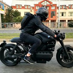 a man riding on the back of a black motorcycle down a street next to tall buildings