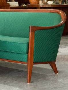 a green couch sitting on top of a cement floor next to a wooden shelf filled with vases