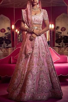 a woman in a pink lehenga standing on a pink couch and posing for the camera