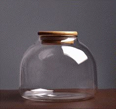 a clear glass jar with a wooden lid on a brown table top next to a gray wall