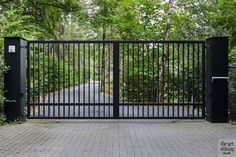 an iron gate in front of a brick walkway surrounded by trees and shrubbery on either side