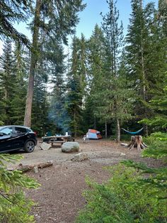 there is a car parked in the woods next to a tent and campfire area